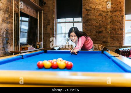 Una giovane donna prende di mira le palle da biliardo durante una partita amichevole di biliardo Foto Stock