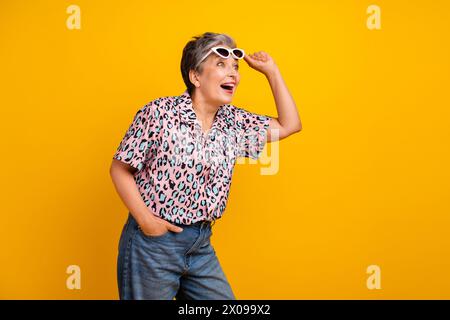 Foto di un'adorabile donna anziana che toglie gli occhiali da sole look da shock negli spazi vuoti indossa un elegante capo con stampa leopardata isolato su sfondo giallo Foto Stock