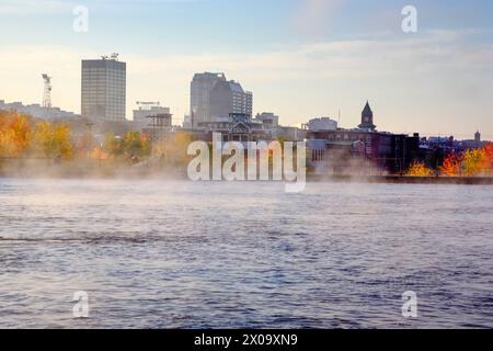 Manchester, New Hampshire USA in una nebbiosa giornata autunnale dal fiume Merrimack. Foto Stock