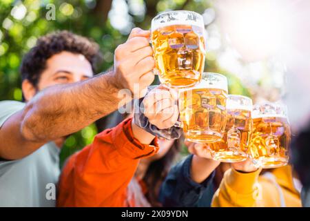 Saluti all'amicizia - gli amici alzano tazze da birra in un brindisi all'aperto, crogiolandosi al sole e condividendo risate, celebrando il cameratismo con lo sfondo Foto Stock