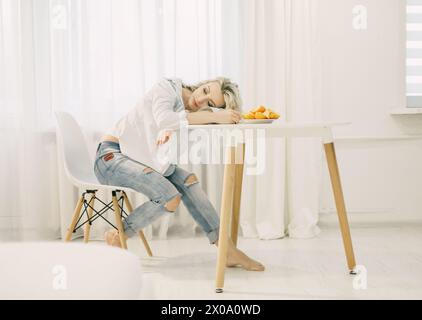 Una donna seduta a un tavolo, con un piatto pieno di frutta di fronte a lei. Foto Stock