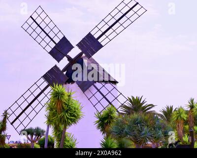 Un mulino a vento bianco a Fuerteventura con palme in primo piano. Primo piano. Foto Stock