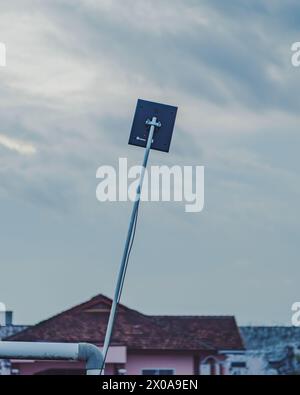 Questa immagine presenta una piccola antenna televisiva digitale montata su un palo metallico di fronte a una casa di periferia. Un cielo blu trasparente riempie lo sfondo. TH Foto Stock