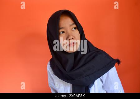 Una donna asiatica indossa con sicurezza un hijab nero su sfondo arancione Foto Stock