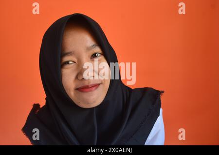 Una donna asiatica indossa con sicurezza un hijab nero su sfondo arancione Foto Stock