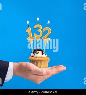 Cupcake per il compleanno a mano - candela numero 132 su sfondo blu Foto Stock