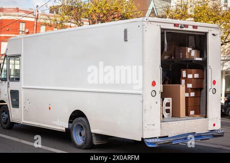 Scattata su una strada cittadina, questa immagine mostra un furgone bianco nordamericano con le sue porte posteriori aperte, che rivela una serie di pacchi pronti per la consegna Foto Stock