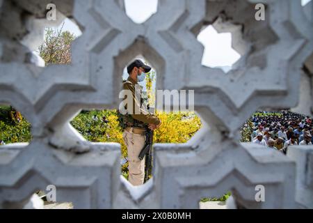 Srinagar, India. 10 aprile 2024. Un poliziotto indiano sta in guardia mentre i musulmani Kashmiri offrono preghiere Eid-al-Fitr fuori da una moschea a Srinagar. Il festival EID-al-Fitr segna la fine del santo mese di digiuno del Ramadan. Nel frattempo, le autorità indiane hanno impedito alle persone di offrire preghiere Eid-al-Fitr nella storica grande Moschea del Kashmir, o Jamia Masjid, per il quinto anno consecutivo nel centro di Srinagar. Credito: SOPA Images Limited/Alamy Live News Foto Stock