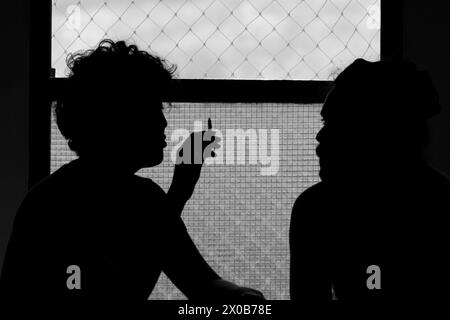Coppia che parla e fuma in una splendida scena davanti alla finestra con una silhouette in bianco e nero Foto Stock