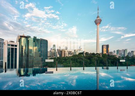Splendida vista sul tetto della città di Kuala Lumpur e di Menara Kuala Lumpur, vicino al tramonto, con la piscina a sfioro del bar sul tetto blu in primo piano e il cielo blu punteggiato Foto Stock