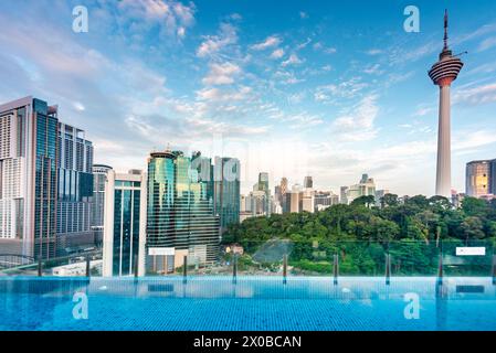 Splendida vista sul tetto della città di Kuala Lumpur e di Menara Kuala Lumpur, vicino al tramonto, con la piscina a sfioro del bar sul tetto blu in primo piano e il cielo blu punteggiato Foto Stock