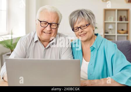 Allegra coppia anziana in pensione che utilizza un notebook per guardare film, fare shopping online e videochiamare. Foto Stock
