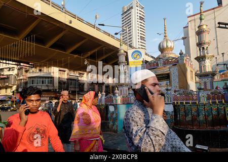 Tre uomini musulmani a Mumbai, in India, che camminano lungo una strada nella zona di Dongri dominata dai musulmani e parlano al telefono cellulare Foto Stock