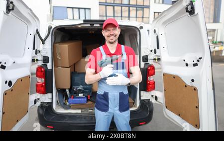 Costruttore sorridente che tiene il trapano vicino all'auto. Concetto di riparazione Foto Stock