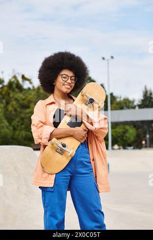 Una giovane donna afro-americana con capelli afro sapientemente in equilibrio su uno skateboard in uno skate Park all'aperto. Foto Stock