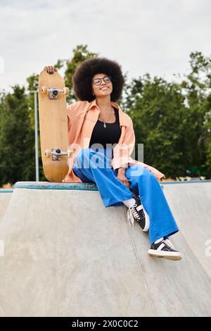 Una giovane donna afroamericana con i capelli ricci si siede in cima a una rampa per skateboard. Trasuda fiducia e determinazione. Foto Stock