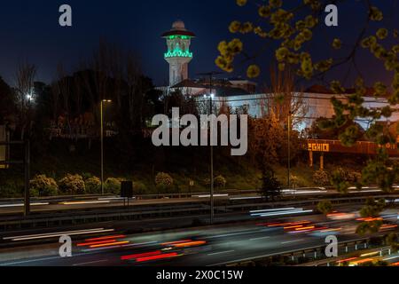 Una maestosa moschea bianca con un torreggiante minareto illuminato perfora il cielo notturno, con le sue finestre che si illuminano di luce calda. Dopo il Ramadan. Colore verde Foto Stock