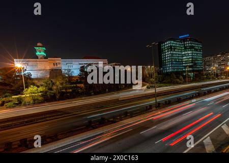 Una maestosa moschea bianca con un torreggiante minareto illuminato perfora il cielo notturno, con le sue finestre che si illuminano di luce calda. Dopo il Ramadan. Colore verde Foto Stock