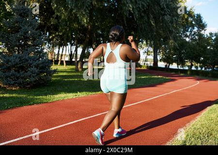 Una donna afroamericana in abbigliamento sportivo corre lungo una pista rossa, mostrando positività corporea e atletismo. Foto Stock