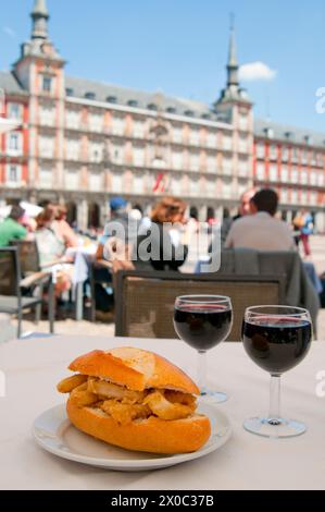 Calamari fritti in sandwich con due bicchieri di vino rosso in una terrazza. La piazza principale di Madrid, Spagna. Foto Stock