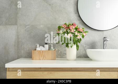 Vaso con bellissimi fiori dell'Alstroemeria e articoli da toeletta vicino al lavandino in bagno Foto Stock