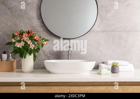 Vaso con bellissimi fiori dell'Alstroemeria e articoli da toeletta vicino al lavandino in bagno Foto Stock