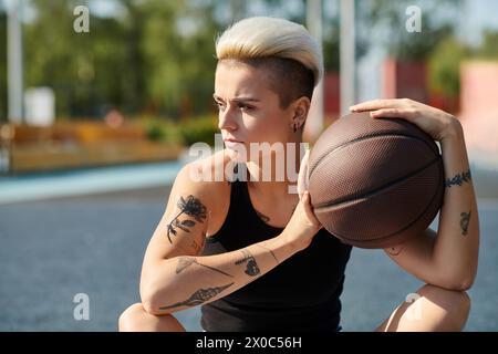 Una giovane donna con i capelli corti e i tatuaggi si siede per terra, nel profondo del pensiero mentre tiene in mano un pallacanestro. Foto Stock