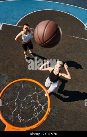 Due giovani donne, amiche, giocano a basket su un campo, mostrando le loro abilità atletiche in una partita estiva a canestro. Foto Stock