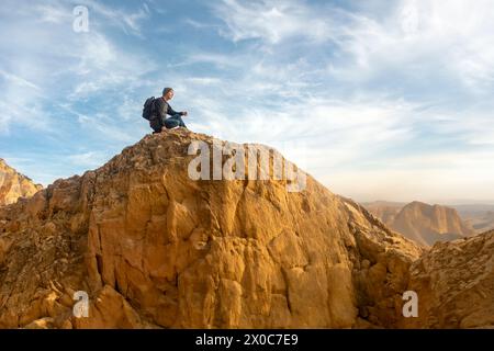 Escursionista maschile seduto sulla cima di una montagna rocciosa che guarda il panorama Foto Stock