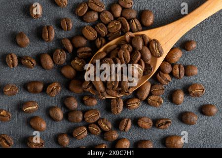 Un cucchiaio pieno di chicchi di caffè tostati su sfondo nero, vista dall'alto Foto Stock