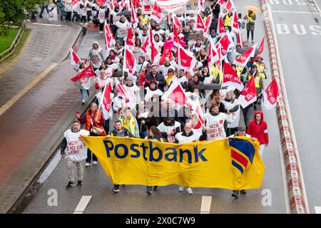 Amburgo, Germania. 11 aprile 2024. I partecipanti a una marcia dimostrativa attraverso il centro di Amburgo durante uno sciopero di avvertimento a Postbank. Lo sciopero fa parte di un'ondata nazionale di scioperi da parte del sindacato Verdi per aumentare la pressione sul datore di lavoro nei negoziati salariali in corso dopo che il terzo ciclo di negoziati si è concluso senza un accordo. Credito: Bodo Marks/dpa/Alamy Live News Foto Stock