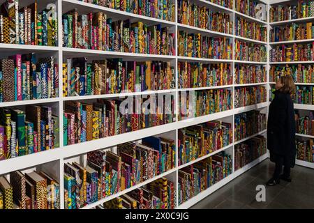 LONDRA, REGNO UNITO - 11 APRILE 2024: un visitatore guarda una nuova installazione su larga scala intitolata "War Library" (2024) composta da 5.000 libri rilegati in stampa a cera olandese che rappresentano conflitti e trattati di pace durante una chiamata fotografica per la mostra "Stati sospesi" di Yinka Shonibare presso Serpentine South a Londra, Regno Unito, l'11 aprile 2024. La prima mostra personale del lavoro di Shonibare in un’istituzione pubblica di Londra da oltre 20 anni esplora temi centrali dei lasciti del potere coloniale, dei siti di rifugio e rifugio, nonché l’impatto ecologico della colonizzazione, l’eredità europea di i Foto Stock