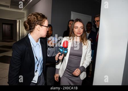 Una donna politica statunitense sicura di sé risponde alle domande della stampa e rilascia un'intervista per i media che camminano nel corridoio dell'edificio governativo. Delegazione americana circondata da una folla di giornalisti. Campagna stampa. Foto Stock