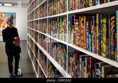 LONDRA, REGNO UNITO - 11 APRILE 2024: un membro dello staff guarda una nuova installazione su larga scala intitolata "War Library" (2024), composta da 5.000 libri rilegati in stampa a cera olandese che rappresentano conflitti e trattati di pace durante una chiamata fotografica per la mostra "Stati sospesi" di Yinka Shonibare a Serpentine South a Londra, Regno Unito, l'11 aprile 2024. La prima mostra personale del lavoro di Shonibare in un'istituzione pubblica di Londra da oltre 20 anni esplora i temi centrali delle eredità del potere coloniale, dei siti di rifugio e rifugio, nonché l'impatto ecologico della colonizzazione, l'eredità europea Foto Stock