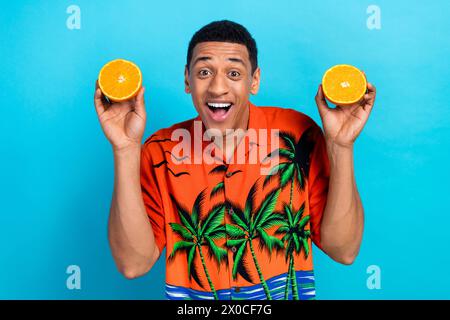 Foto dell'eccitante camicia con stampa vestito da ragazzo che regge due metà arancioni sfondo blu isolato Foto Stock