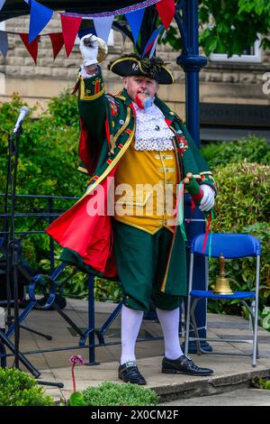 Uomo pigrillo e fattorino (abiti da livrea verde oro) che fa un annuncio pubblico rumoroso - Ilkley, West Yorkshire, Inghilterra, Regno Unito. Foto Stock