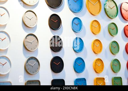 File colorate di orologi rotondi nero blu giallo verde rosso su una parete bianca Foto Stock