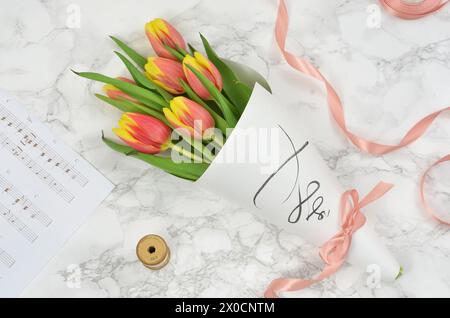 Bouquet di tulipani avvolti in carta con nastro. Spartito di musica, piatto. Foto Stock