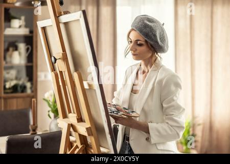 Bella pittrice che si diverte mentre dipinge in uno studio d'arte domestico. Woman Artist lavora sulla pittura acrilica astratta nello studio d'arte. Foto Stock