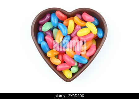 caramelle dolci multicolore in ciotola a forma di cuore su sfondo bianco, vista dall'alto. Spazio per il testo Foto Stock