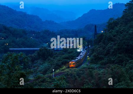 In un'alba nebbiosa di inizio estate a New Taipei City, nella parte settentrionale di Taiwan, un treno locale parte lentamente dalla stazione di Wanggu verso la cascata di Shifen Foto Stock