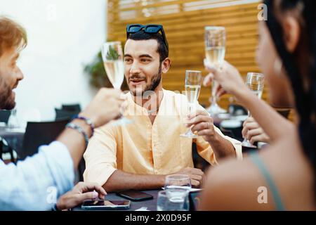 Un allegro gruppo di amici che alzano i bicchieri di champagne in un brindisi - informale festa all'aperto, che incarna la gioia di stare insieme. Foto Stock