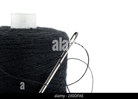 Una bobina con filo nero e un ago su sfondo bianco. Isolamento filettatura. Accessori per cucire. Spazio vuoto per l'iscrizione Foto Stock