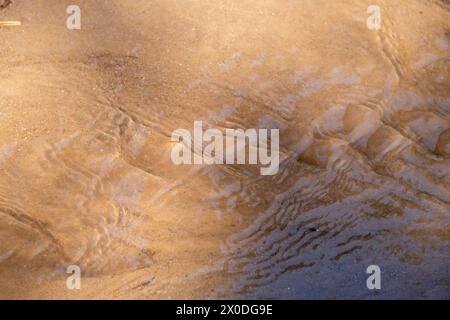 L'acqua si riversa sulla sabbia della spiaggia. Sfondo astratto Foto Stock