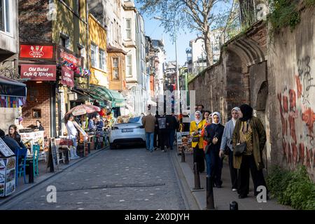 Istanbul, Turchia - 10 aprile 2024, le persone si siedono sulla veranda di un caffè nel distretto di Balata durante il Ramadan. Le ragazze in hijab, vestite in modo intelligente, camminano Foto Stock