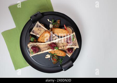 vista dall'alto delicata, midollo osseo cotto con crostini, erbe e spezie su un piatto nero. Foto Stock