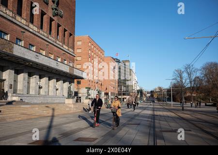 Una coppia in bicicletta, l'altra in scooter, viaggia lungo Rådhusplassen. Centro di Oslo, situato tra il Municipio di Oslo e l'Oslofjord a Vika, Norvegia Foto Stock