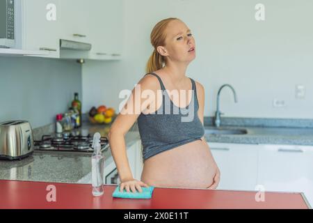 Una donna incinta stanca siede in cucina dopo la pulizia. Salute e vitalità di una donna incinta Foto Stock