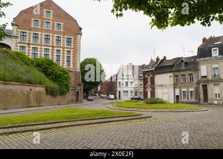 Cambrai, Francia - 21 maggio 2023: Un consistente edificio in mattoni si erge alto su un campo verde vivace sotto un cielo limpido, mostrando il contrasto tra m Foto Stock