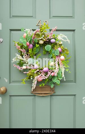 Ghirlanda di Pasqua in plastica kitsch con decorazioni di uova di Pasqua dipinte in pastello artificiali su una porta d'ingresso verde nel Galles Ceredigion Regno Unito KATHY DEWITT Foto Stock